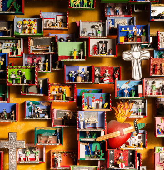 Colorful wall display with miniature scenes, religious symbols, and figures in a storefront setting.