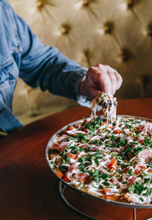 Person serving a loaded pizza with melted cheese, vegetables, and herbs.