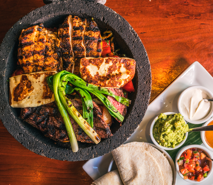 Caliente skillet meal with grilled meats, halloumi, grilled vegetables, tortillas, and sauces.