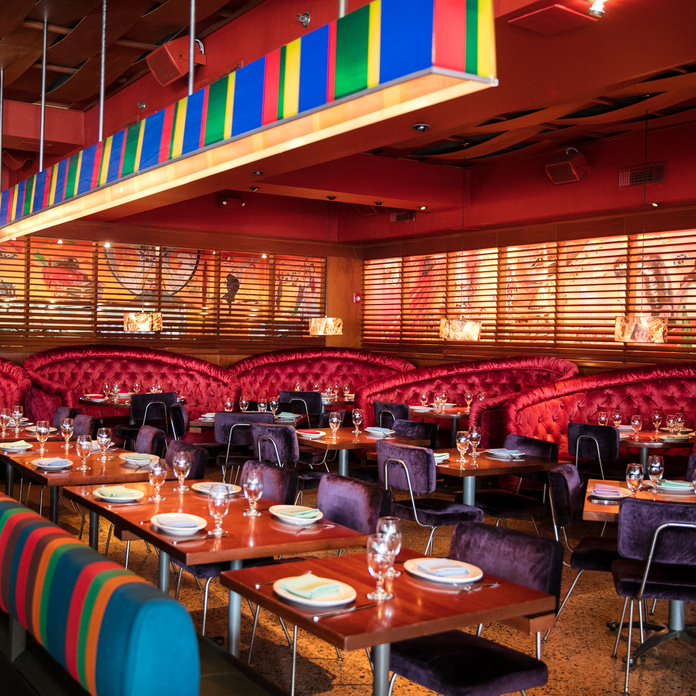 Top-down view of wooden table with vibrant dishes, including steak, sides, and drinks, in a colorful, ornate plate setting.