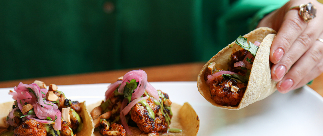 Person holding a tacos filled with grilled cauliflower, pickled onions, and avocado sauce.